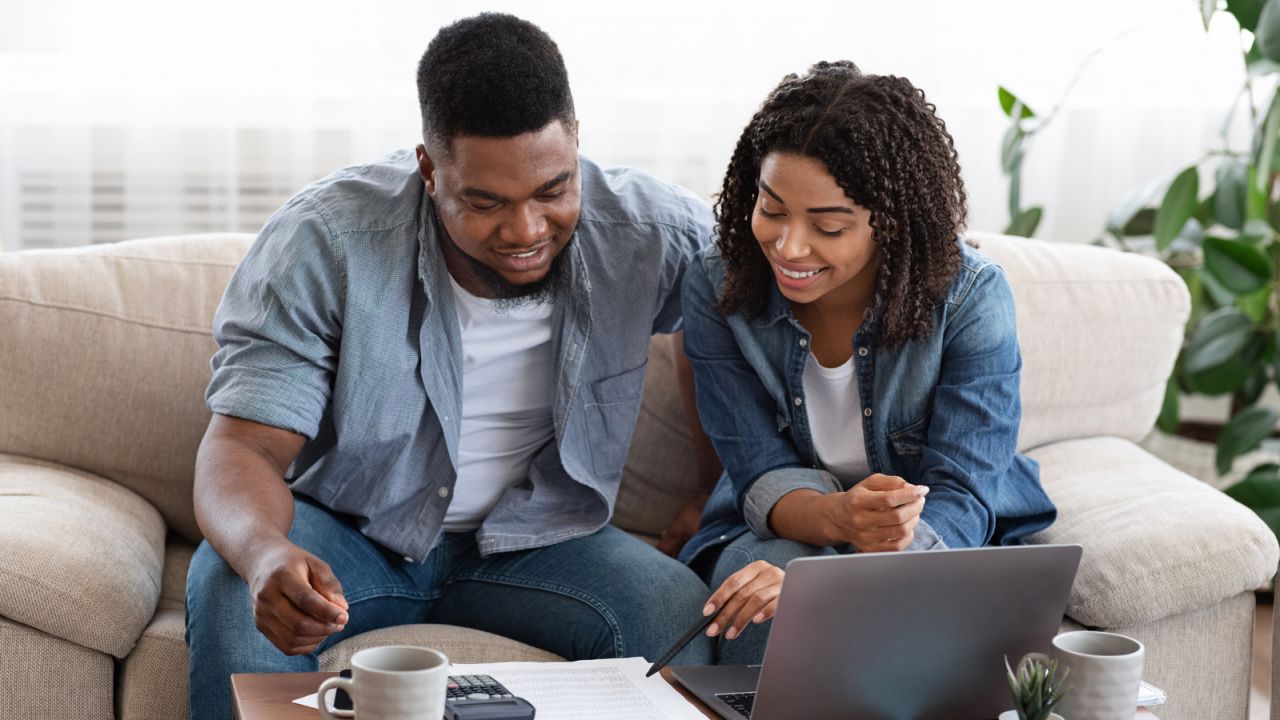 Couple looking down and smiling while sitting on a couch looking at documents.