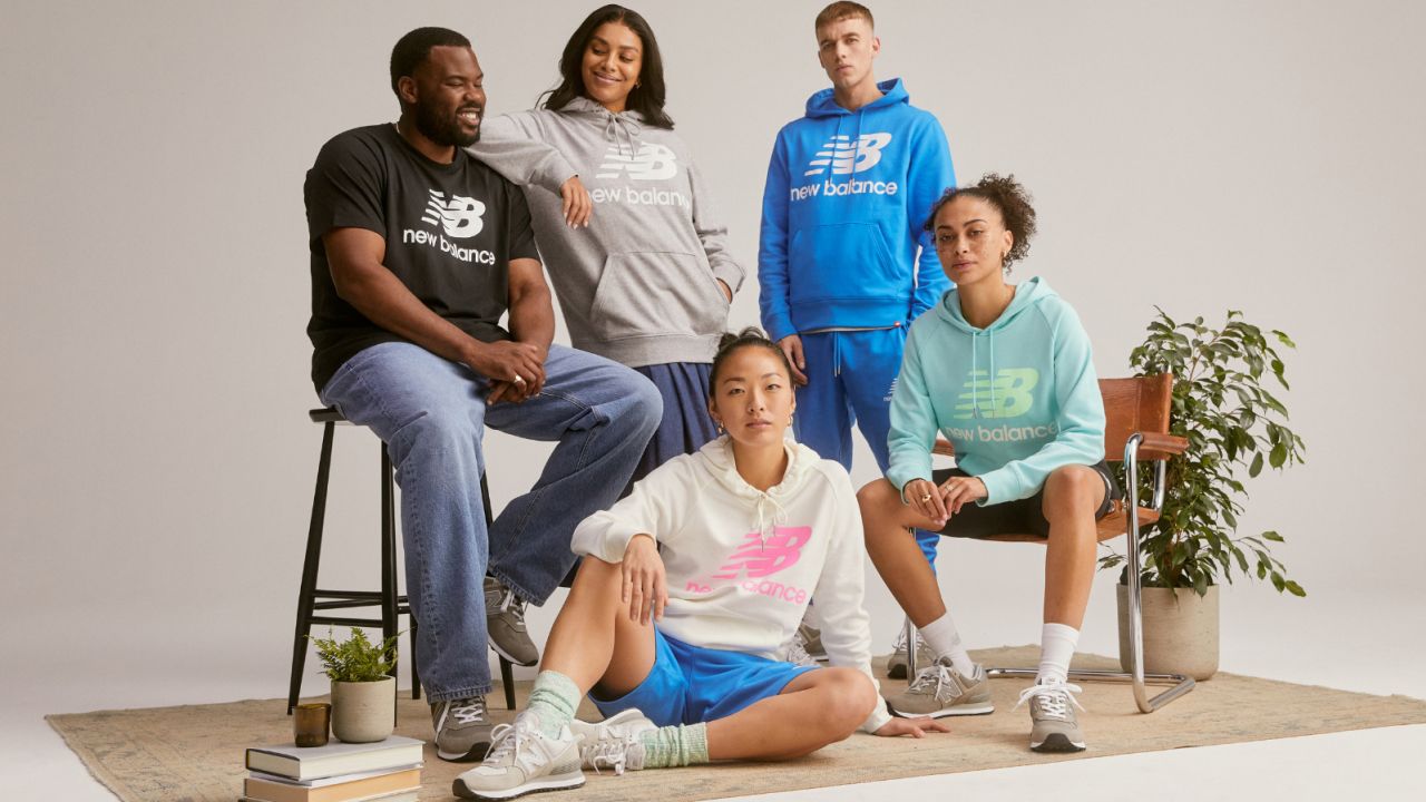 Five people standing and sitting casually while wearing New Balance tops and hoodies.