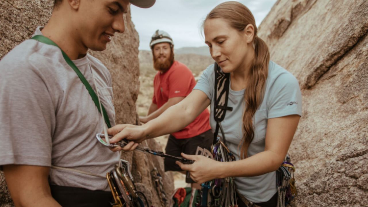 Three people gearing up to climb rocks while wearing Carhartt shirts.