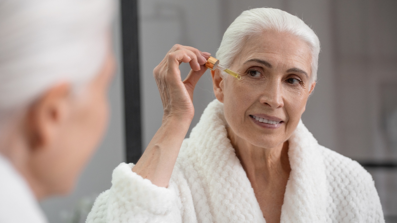Woman in a robe applying serum to her face
