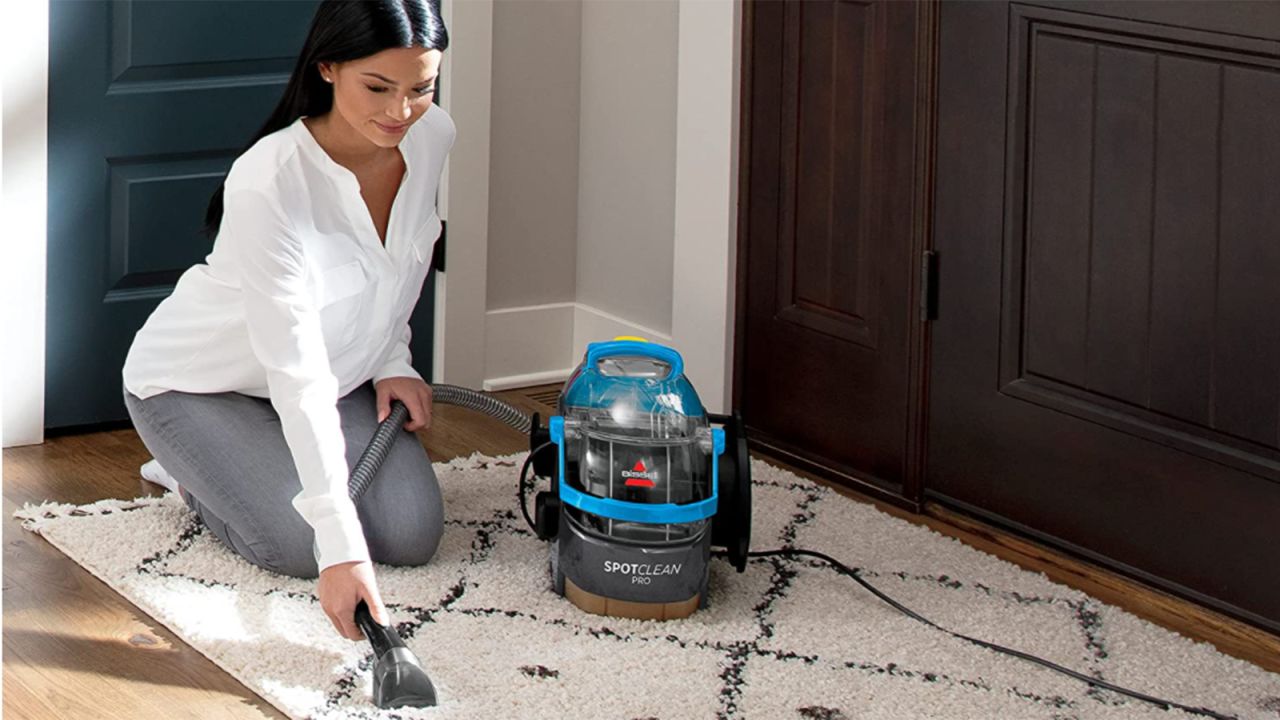 Person on their knees using a carpet cleaner on a rug.